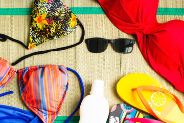 Colorful bikini tops, designed on a wicker surface, with sunglasses and sun oil