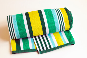 Rolled beach towel in yellow and green colors on white surface