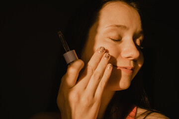 Obraz premium Beautiful white European baby face young woman applying serum from an eyedropper. Facial skin care cosmetic. Daily routine, self-care. Beauty tools.