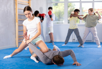 Obraz premium Determined teenage girl learning effective self defence techniques in sparring with male instructor, practicing painful armlock on opponent lying face down on floor in gym..