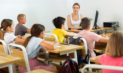 Kids sitting in classroom during lesson. Teacher sitting in front of computer.