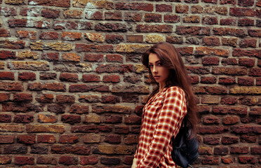 Beautiful brunette woman with long brown hair standing on the old red brick wall building background in casual red shirt on the spring city. Closeup vintage banner - 794518830