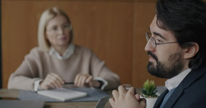 Sad Middle Eastern businessman sharing emotion with female therapist while psychologist writing and listening at desk in office. Therapy session and communication concept.