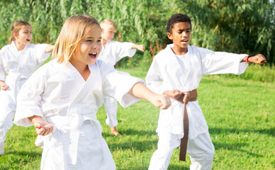 Naklejka na ściany i meble Kids in kimono doing kata moves during outdoor karate training.