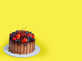 Chocolate cake with fresh berries, strawberry, cherry, blueberry isolated on yellow background. Horizontal orientation