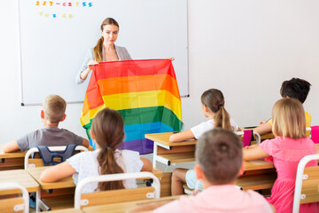 Portrait of smiling young female teacher conducting lesson for tweens, talking about LGBT community and showing rainbow flag