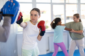 Focused girl hitting the focus mitts held by his boxing trainer