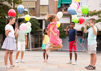 Kids playing with Chinese jumping rope outdoors. They're holding multicolored balloons in hands.