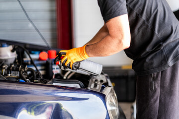 Unrecognizable mechanic and driver in gloves pour oil into car engine, preparing for race.