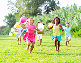 Barefoot children running through field with balloons in hands and smiling.