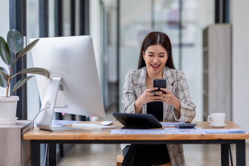 Portrait of young Asian businesswoman in suit, woman smiling and work at workplace inside office, accountant with calculator behind paper phone signing contracts and financial reports	