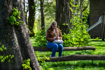 Woman working remotely on her mobile phone in a serene park playground. A woman sitting on park bench, engrossed in sending an email from her smartphone