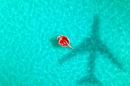 Shadow of airplane and happy woman on inflatable ring in swimming pool, aerial view. Summer vacation
