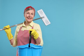 Happy housewife with mop and bucket on light blue background, space for text