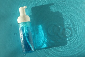 Bottle of cosmetic product in water on turquoise background, top view. Space for text