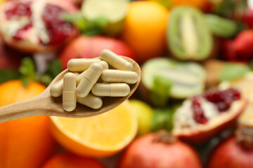 Vitamin pills in spoon against fresh fruits, closeup. Space for text