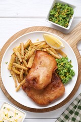 Tasty fish, chips, sauce, peas and lemon on white wooden table, top view