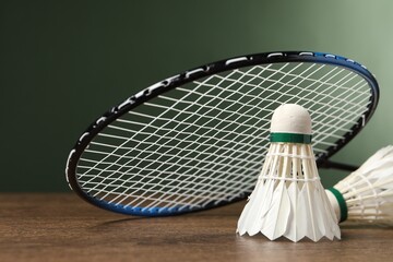 Feather badminton shuttlecocks and racket on wooden table against green background, closeup. Space for text