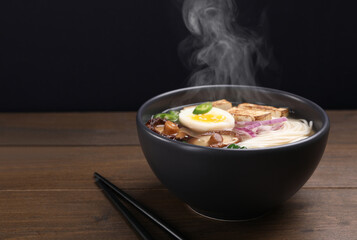 Delicious hot vegetarian ramen in bowl on wooden table against black background, closeup. Space for text
