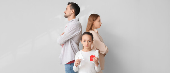 Sad little girl with family figure and her parents on light background. Divorce concept