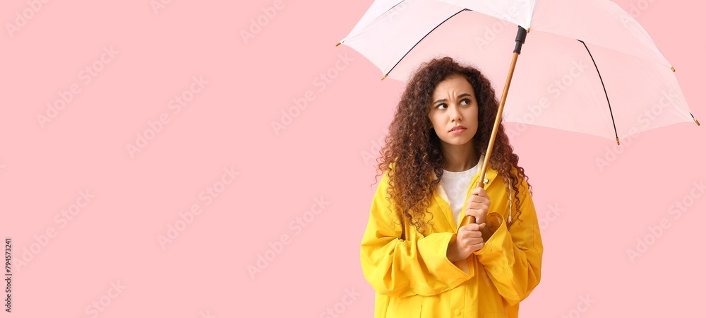 Poster Worried young African-American woman in raincoat holding umbrella on pink background with space for text