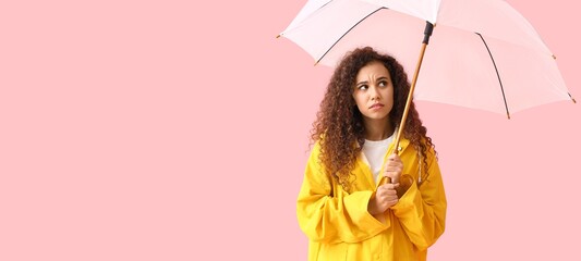Worried young African-American woman in raincoat holding umbrella on pink background with space for...