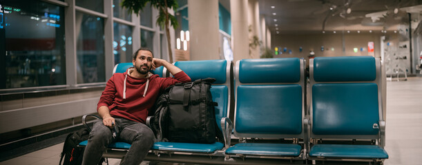 A young man is waiting to board a plane with hand luggage at the airport at the gate at night.
