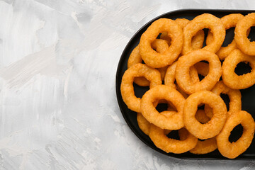 Plate with fried breaded onion rings on grey background