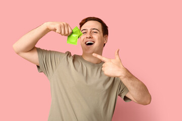 Happy young man pointing at condoms on pink background. Safe sex concept