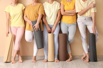 Group of mature women with yoga mats near beige wall