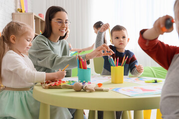 Cute little children with nursery teacher drawing at table in kindergarten
