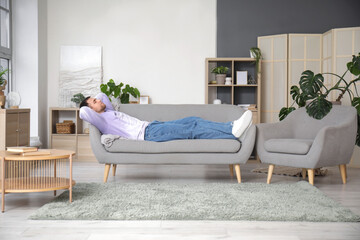 Young man napping on grey sofa at home