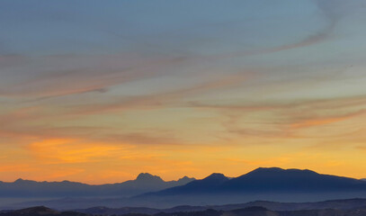 Luminoso tramonto arancio e ocra sopra le montagne italiane