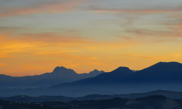 Luminoso tramonto arancio e ocra sopra le montagne italiane