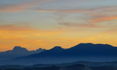 Luminoso tramonto arancio e ocra sopra le montagne italiane