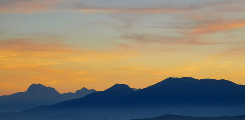 Luminoso tramonto arancio e ocra sopra le montagne italiane