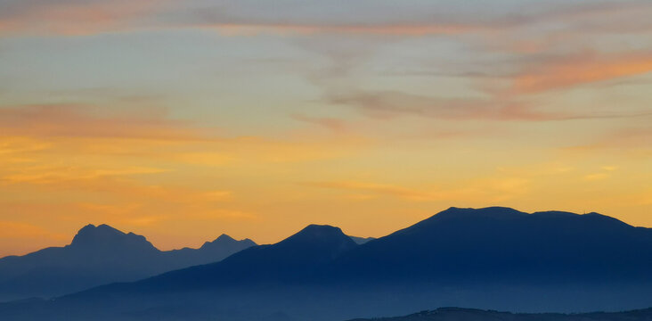 Luminoso tramonto arancio e ocra sopra le montagne italiane
