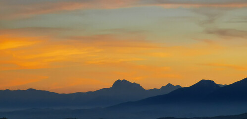 Fototapeta na wymiar Luminoso tramonto arancio e ocra sopra le montagne italiane