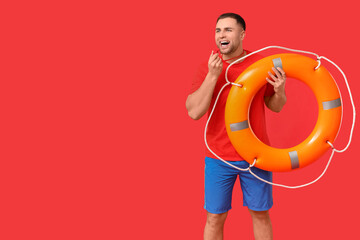 Happy young lifeguard with lifebuoy and whistle on red background