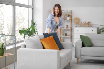 Happy young woman putting pillow on sofa at home