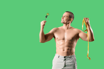 Male bodybuilder with tape measure and cucumber on green background