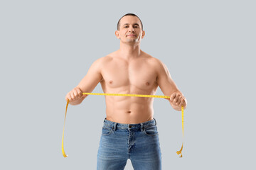 Male bodybuilder with tape measure on light background