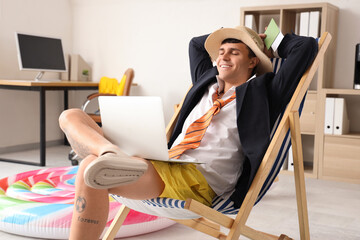 Young businessman with laptop ready for summer vacation in office