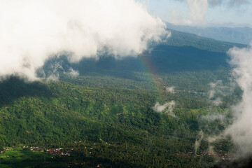 Aerial View of Lush Green Forests and Hills with Clouds and a Faint Rainbow.