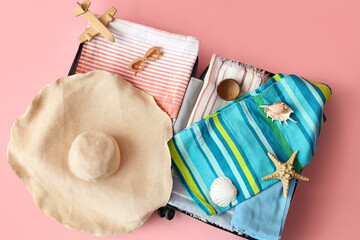 Open suitcase with beach accessories, toy plane and seashells on pink background