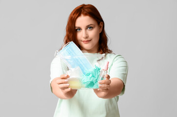Beautiful young woman holding bag with rubber gloves, mask and sanitizer products on grey background