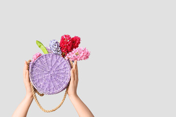 Female hands with lilac flowers in stylish wicker bag on grey background