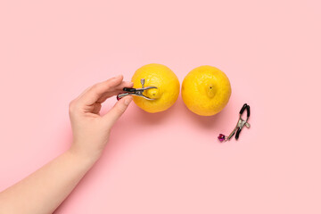 Female hands with lemons and nipple clamps on pink background. Sex education