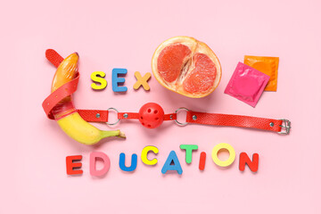Text SEX EDUCATION with condoms, fresh fruits and mouth gag on pink background
