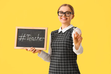 Young woman holding chalkboard with hashtag and word TEACHER on yellow background